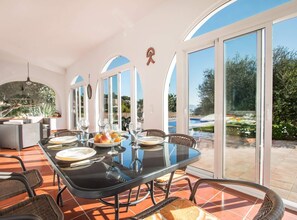 Un espace repas comprenant une grande table, des chaises et donnant sur une piscine.