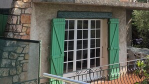 A two-story building with a stone facade, green shutters, and a balcony with wrought iron railings.