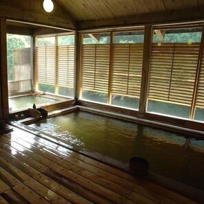 A wooden room with a hot tub, large windows with blinds, and a wooden floor.