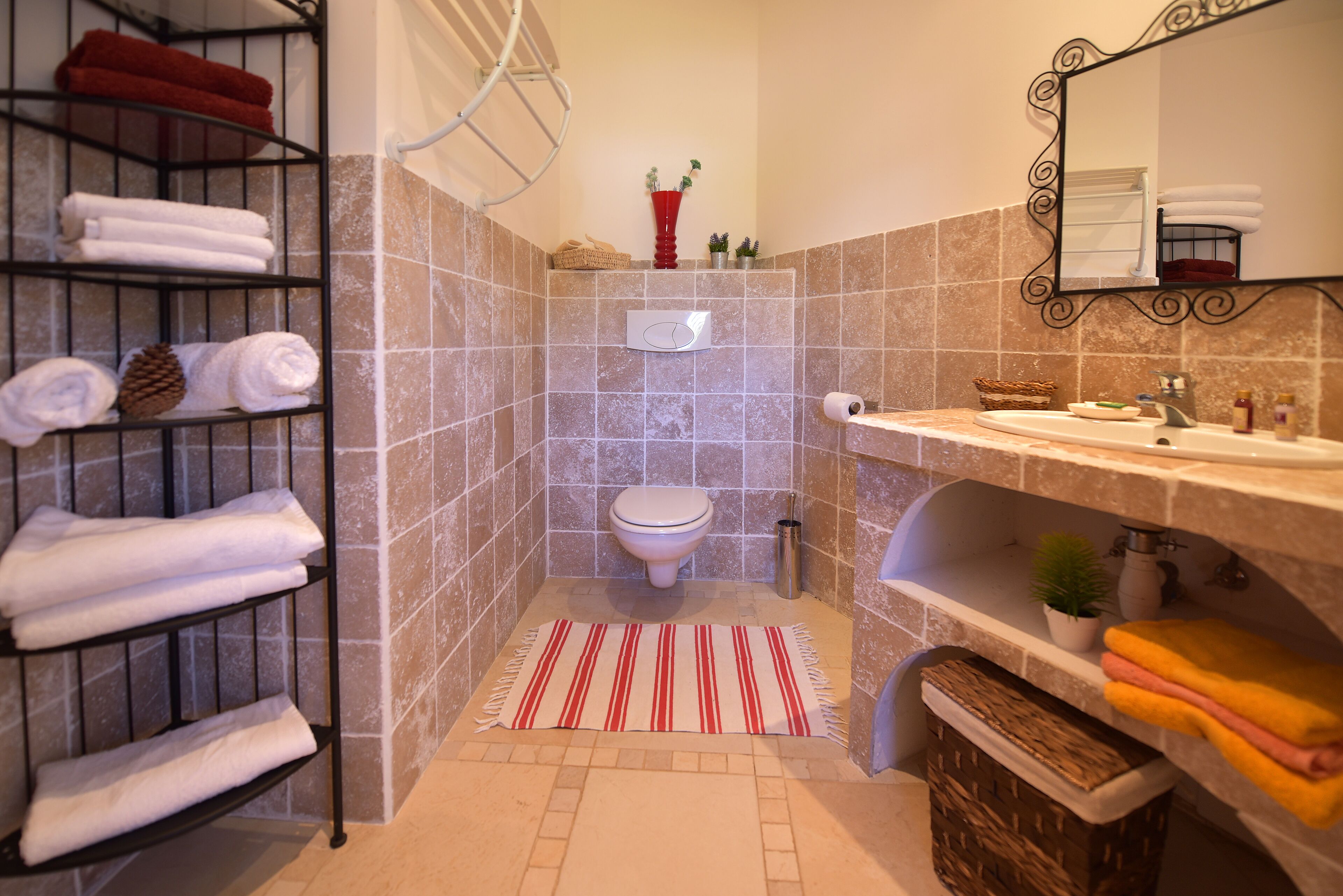 A bathroom with a tiled shower area, a toilet, a sink with a mirror, and a towel rack with neatly folded towels.