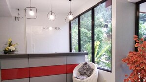 Un comptoir d'accueil au design moderne, un fauteuil en osier et une grande fenêtre donnant sur un paysage verdoyant.