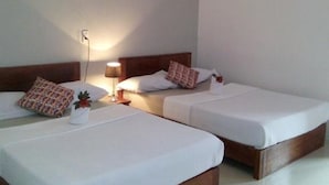 Une chambre d’hôtel avec deux lits simples, une table de chevet avec une lampe, un climatiseur fixé au mur et un petit objet décoratif sur le lit situé à gauche.
