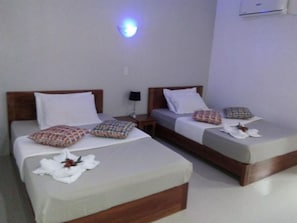 Two single beds with wooden headboards, white linens, patterned pillows, and a small table with a lamp between them. - La Casa Teresa Beach Resort (El Nido)