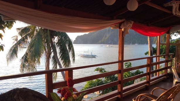 Une terrasse en bois offrant une vue sur la mer, des palmiers et un bateau au loin.