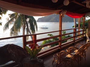 A wooden deck with a view of the sea, palm trees, and a boat in the distance. - La Casa Teresa Beach Resort (El Nido)