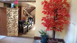 Un couloir avec un mur en pierre, un escalier, un coin repas et une plante en pot aux feuilles rouges.