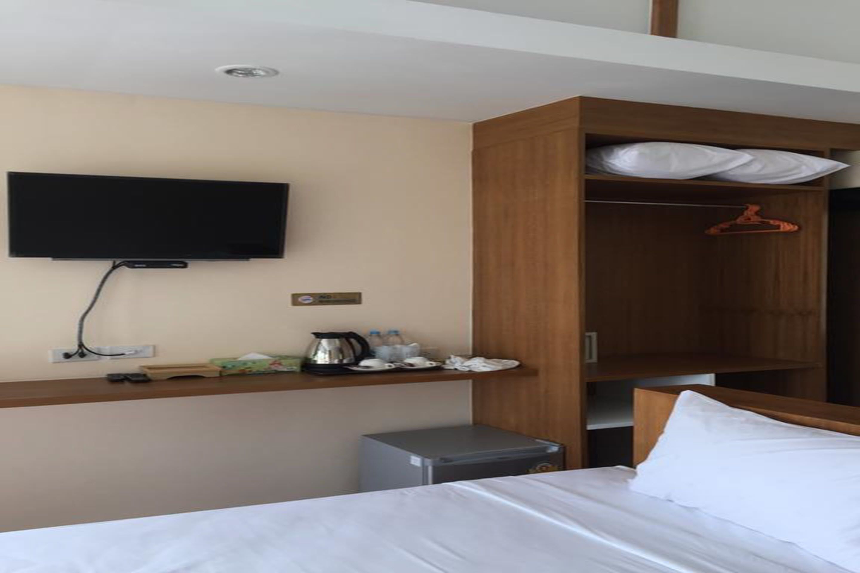 Habitación de hotel con cama, televisor montado en la pared, armario de madera y una mesita con tetera y tazas.