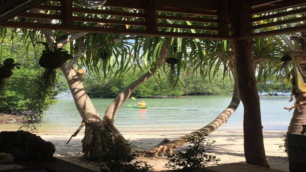 A beach with a wooden structure, palm trees, and a kayak on the water.