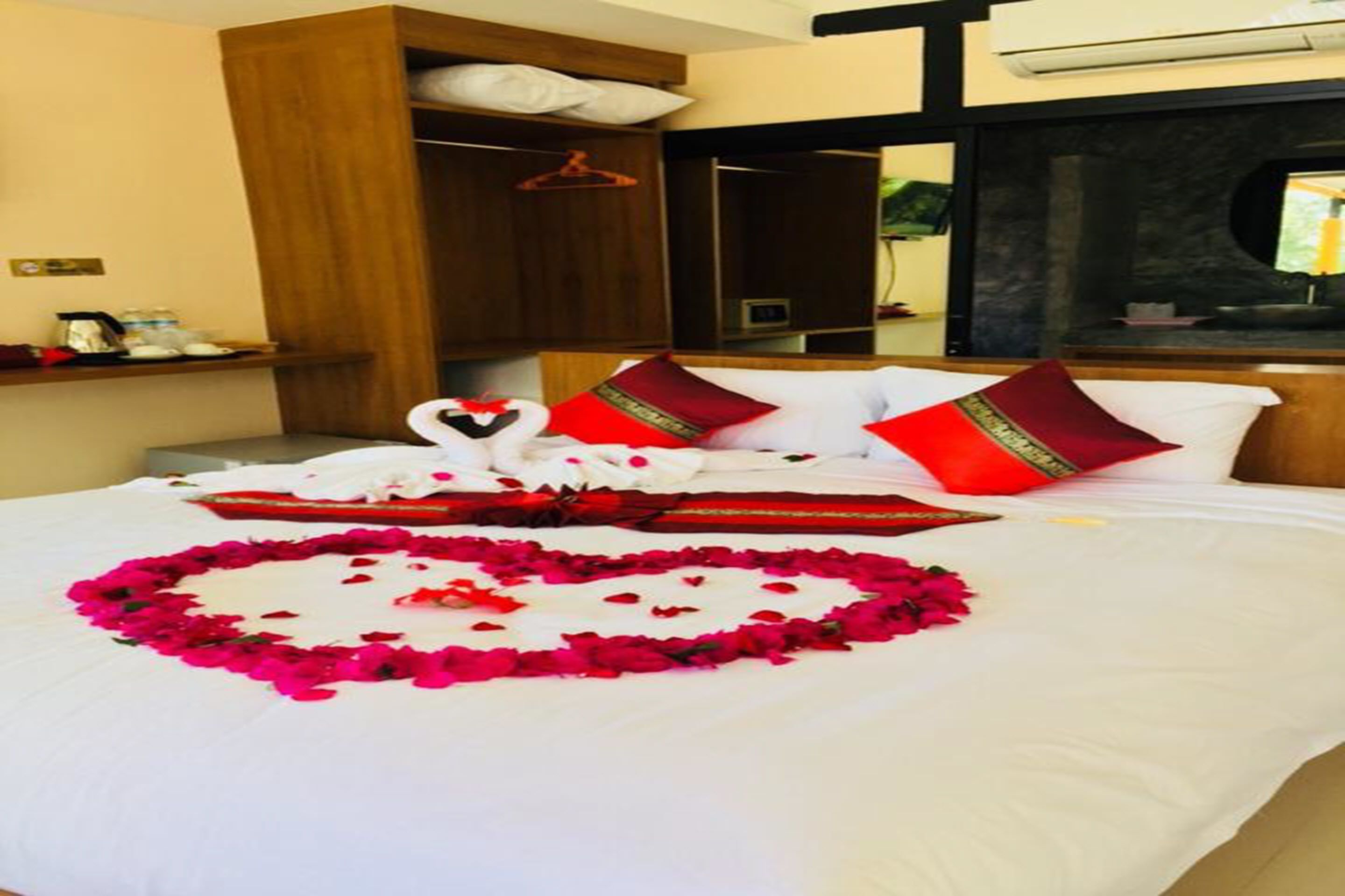 Quarto de hotel com cama bem arrumada, um arranjo de pétalas de rosa em formato de coração e uma decoração de cisne.