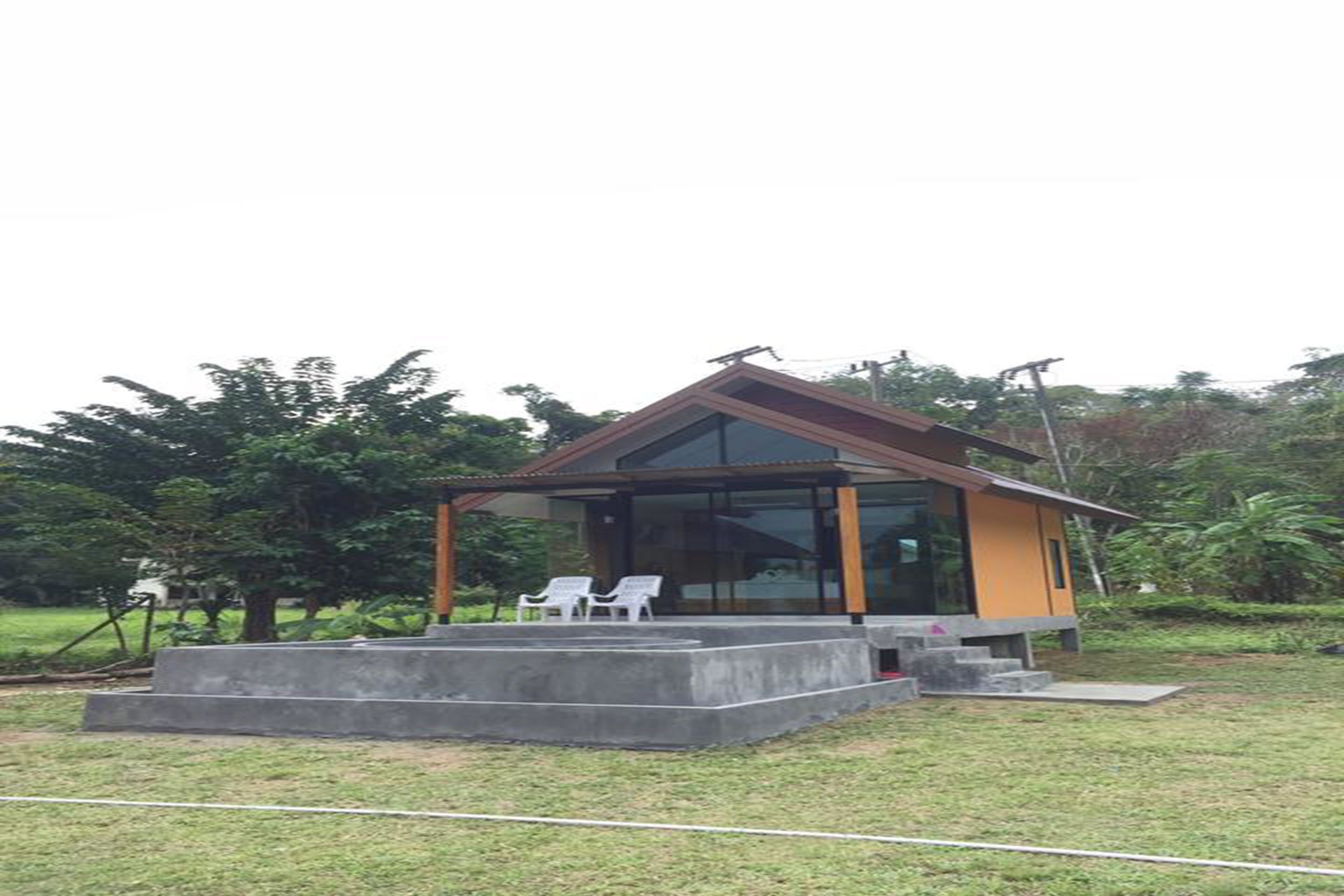 Una casa moderna con fachada de vidrio, techo de madera y una plataforma de concreto con dos sillas blancas.