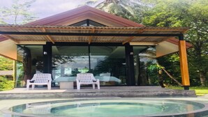 A covered outdoor area with a pool, two white chairs, and a table.