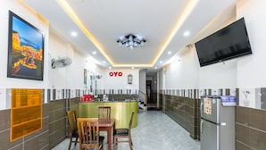A hotel lobby with a reception desk, a dining area with chairs and a table, a refrigerator, and a TV mounted on the wall. - Bong House Homestay Hoi An (Da Nang)