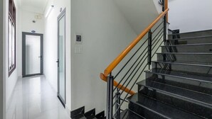 A modern staircase with black steps and a wooden handrail, leading to an interior space with white walls and a door. - Bong House Homestay Hoi An (Da Nang)