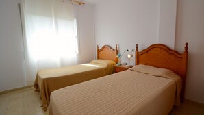 Un dormitorio con dos camas, cabeceros de madera, una mesita de noche con una lámpara y una ventana con cortinas.