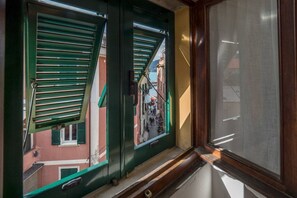 Una ventana con contraventanas verdes, vista a una calle estrecha con edificios, y un marco de madera.