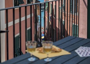 Un balcon donnant sur une rue étroite, deux verres de bière et une carte à jouer posée sur une table.