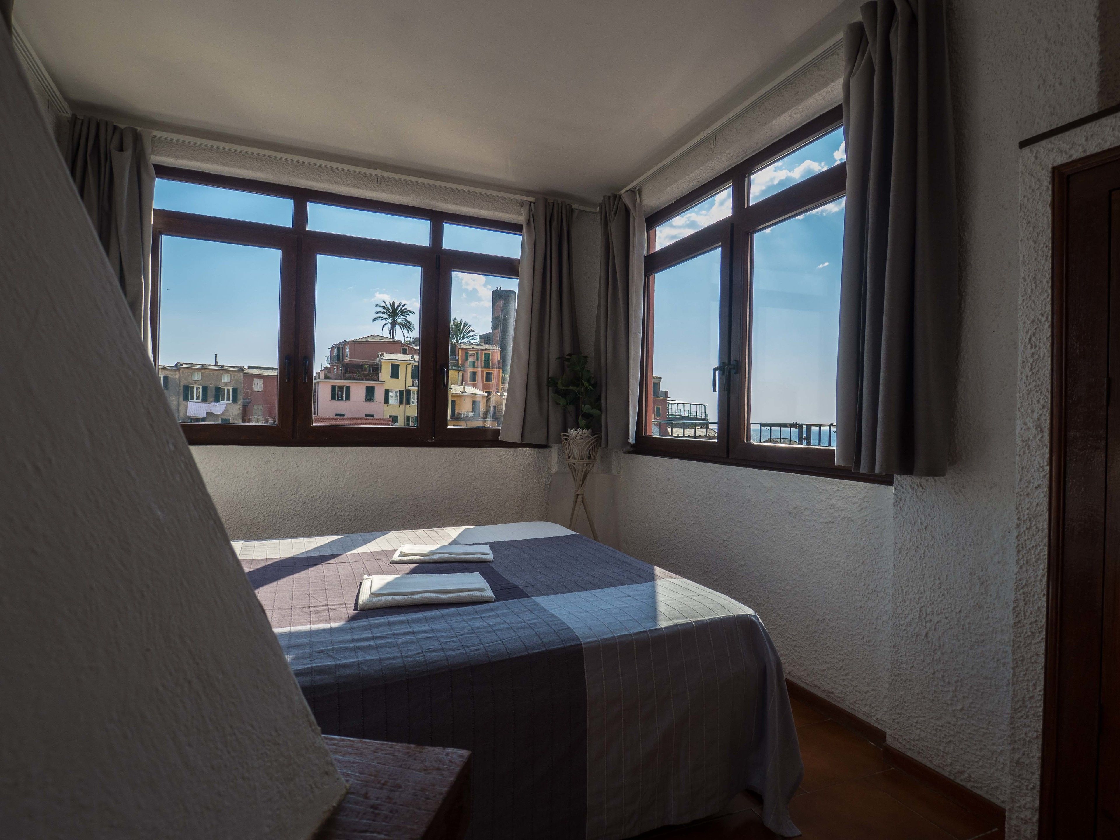 Ein Zimmer mit einem Bett, großen Fenstern und Blick auf Gebäude.