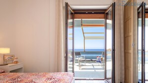 A hotel room with a bed, a nightstand, a view of the sea through an open door, and a balcony with chairs and a table. - ClickSardegna Penthouse Valencia with Sea-View Terraces, Close to the Beaches (Alghero)