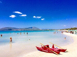 A beach with clear turquoise water, a red boat, and a mountainous backdrop. - ClickSardegna Penthouse Valencia with Sea-View Terraces, Close to the Beaches (Alghero)