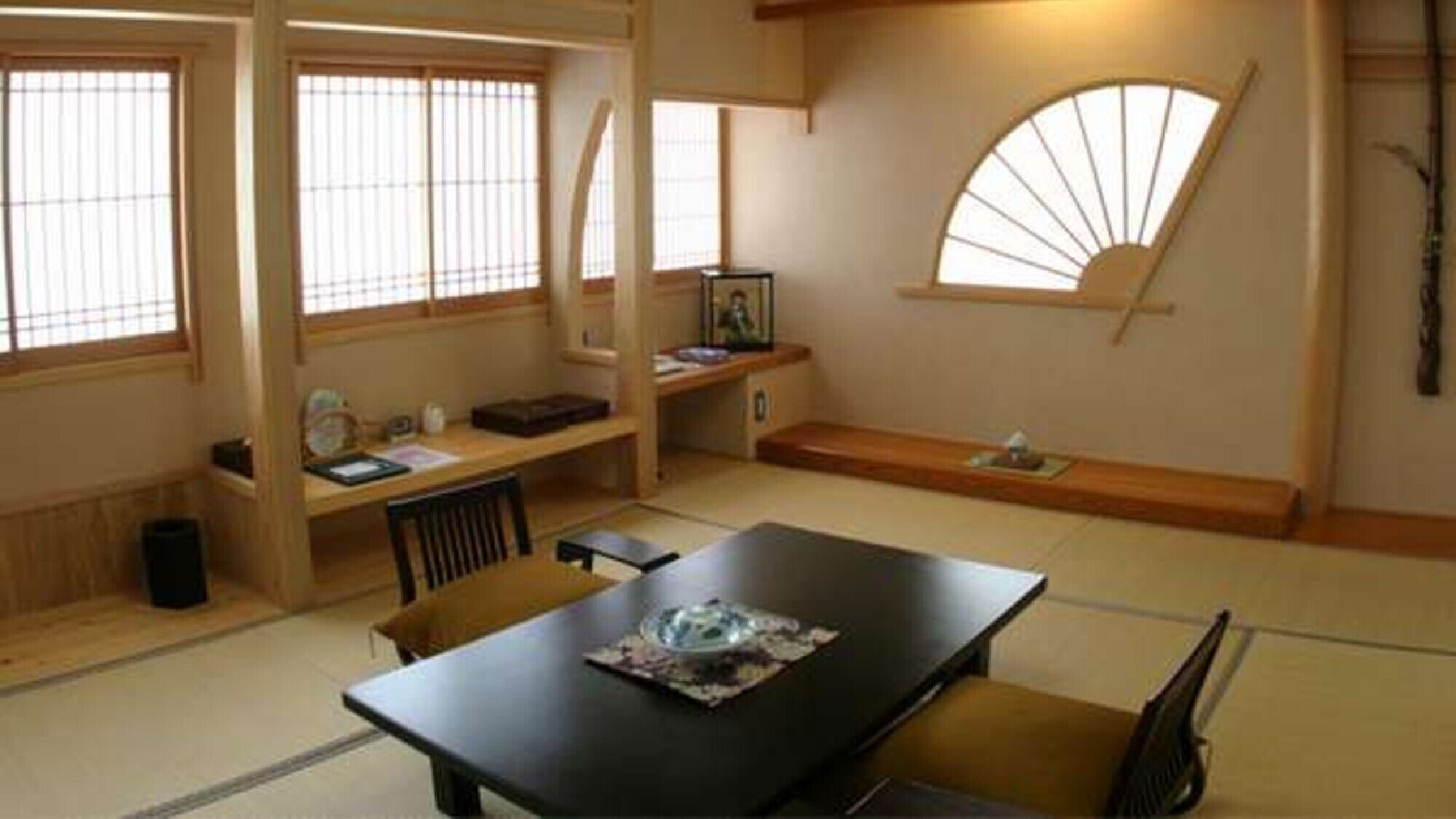 Una habitación japonesa tradicional con suelo de tatami, una mesa baja con cojines, una puerta corredera y un abanico en la pared.