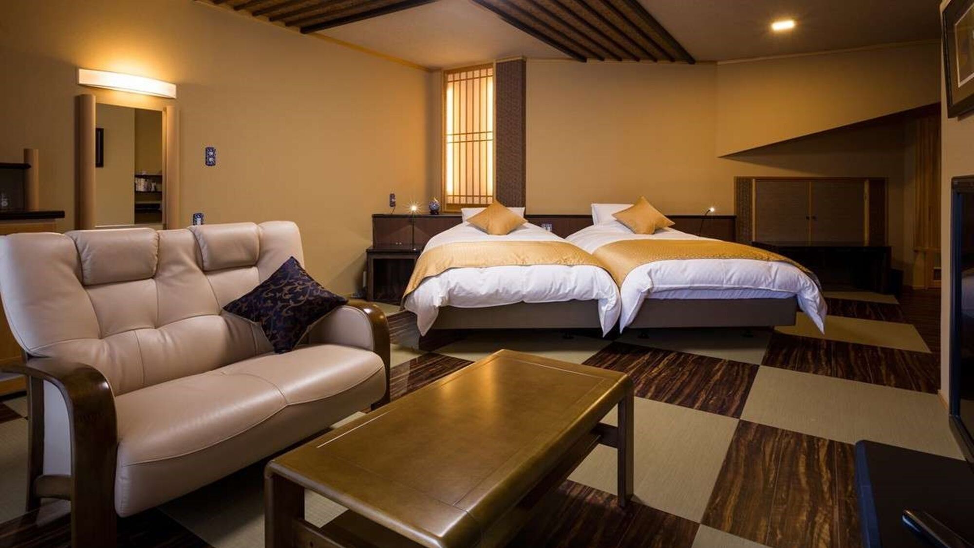 Habitación de hotel con sofá, dos camas, una mesita de noche, una lámpara y una mesa de centro de madera.