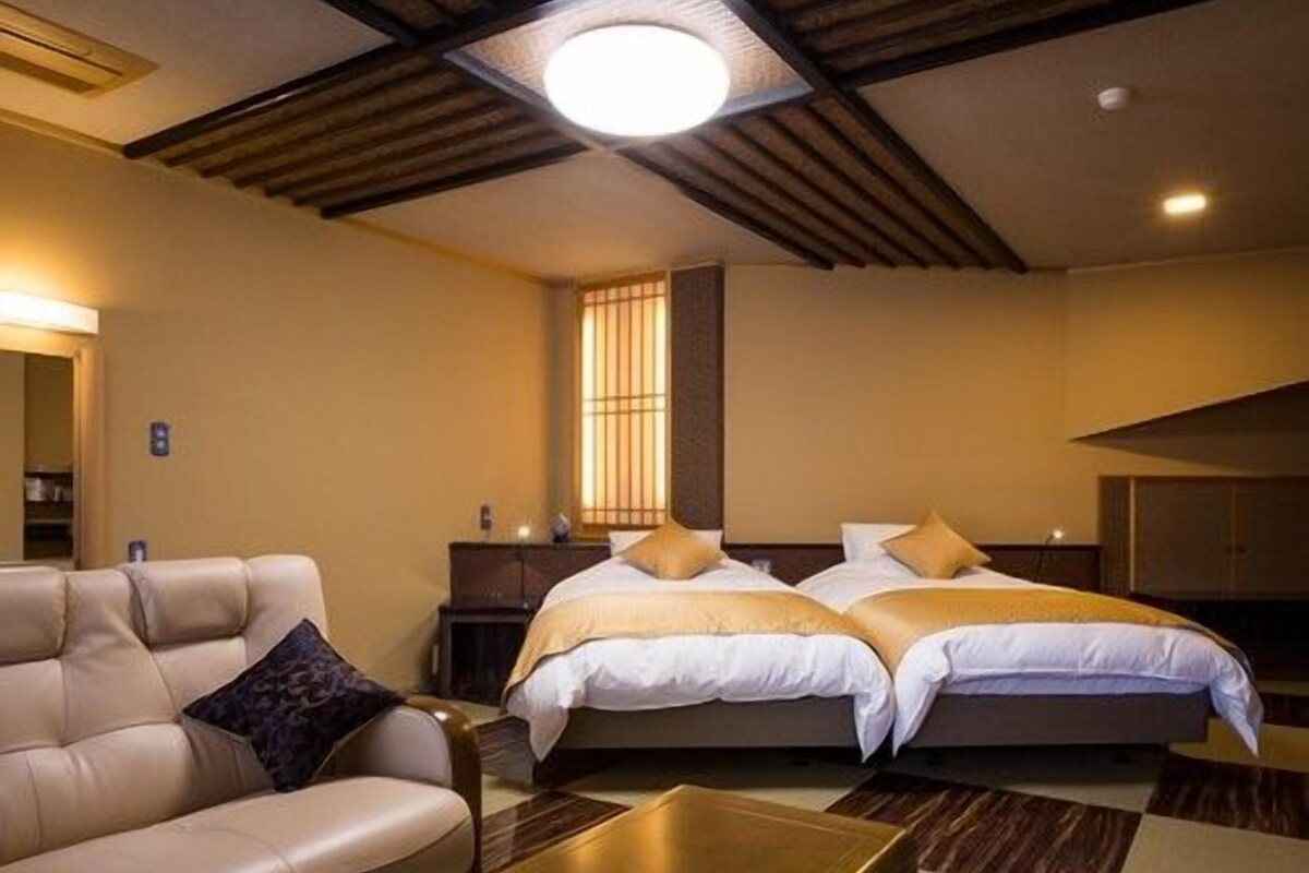 Una habitación de hotel con sofá, dos camas, una mesita de noche y una lámpara en el techo.