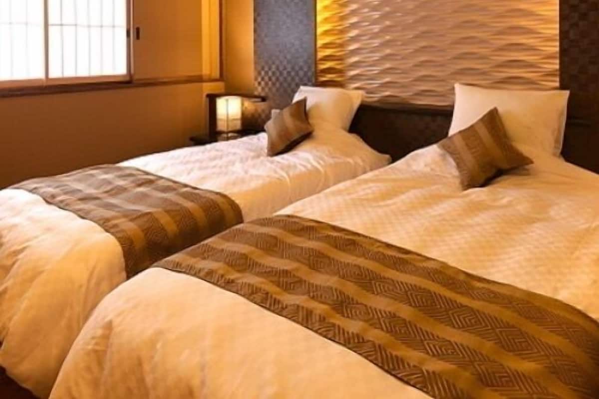 Hotellihuone, jossa on kaksi sänkyä, suuri ikkuna ja kuvioitu seinä.