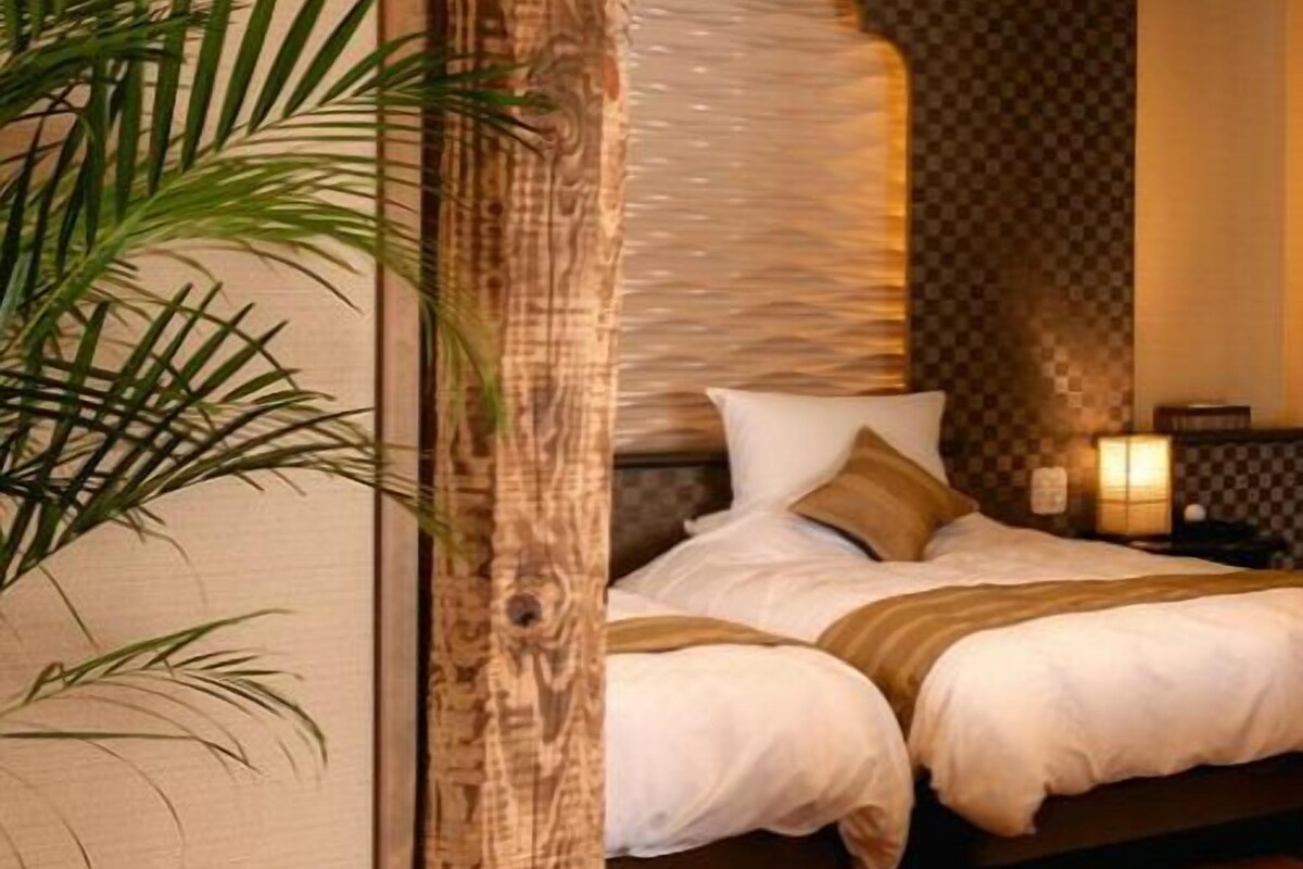 A bedroom with a bed, a nightstand, a lamp, and a potted plant.