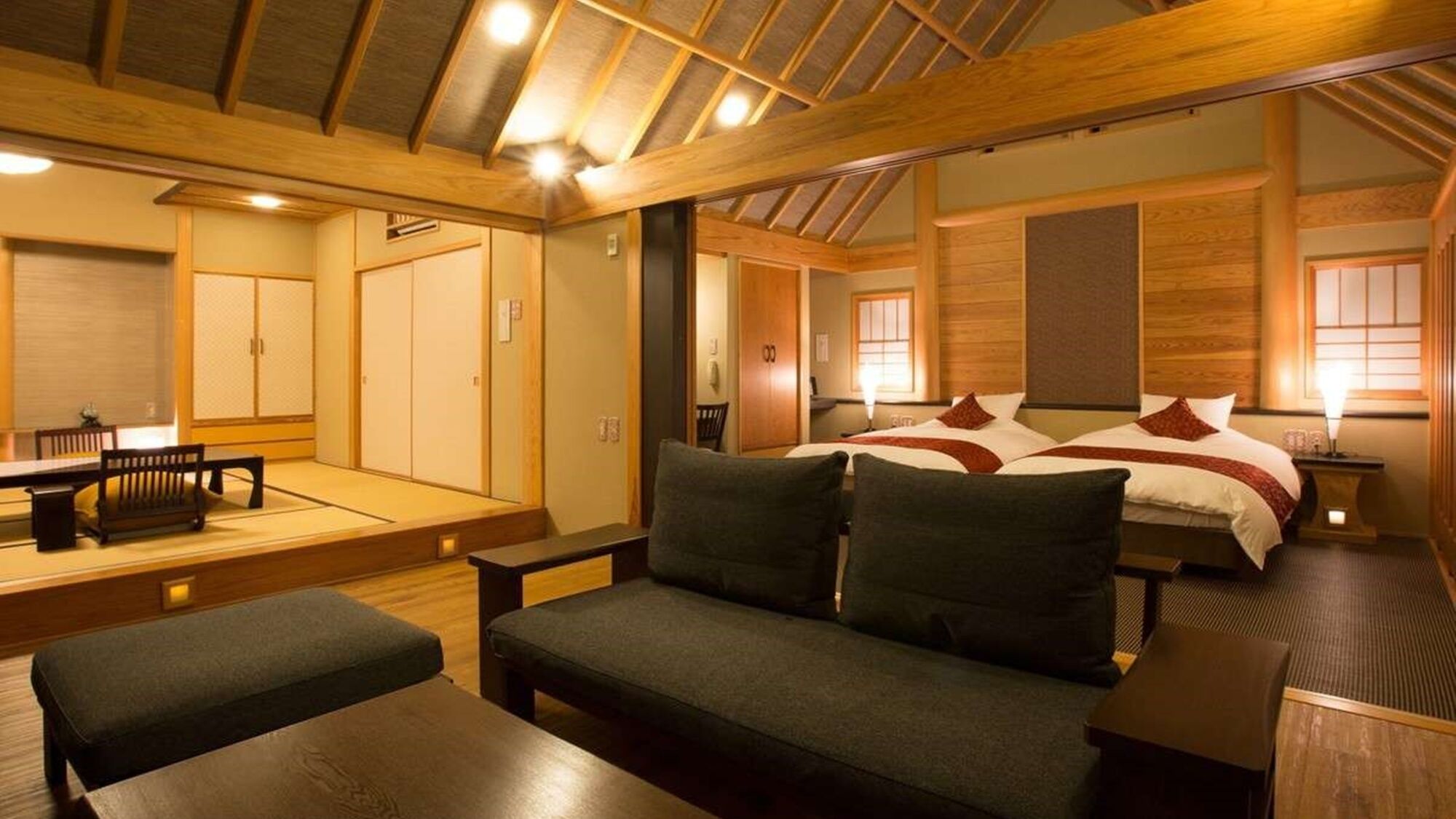 Una habitación al estilo japonés tradicional, con suelo de tatami, una mesa baja, un sofá y una cama con detalles en rojo.