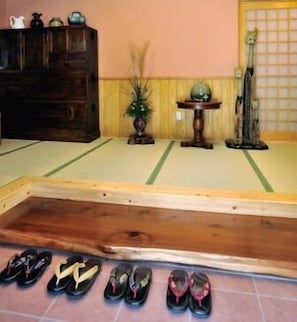 A tatami mat room with a wooden bench, a small table with a vase, and a statue. - Ryojouen Yamazato (Takachiho)