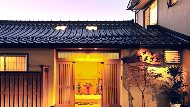 Um edifício tradicional japonês com telhado de telhas, entrada de madeira e uma placa com caracteres japoneses.