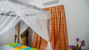 A bedroom with a bed covered by a white canopy, a window with orange curtains, and a wall-mounted air conditioner. - senu villa (Bope-Poddala)