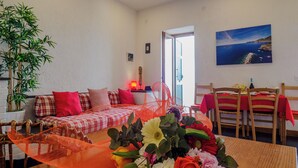 A cozy living room with a sofa, dining table, and chairs. There is a plant, a lamp, and a painting on the wall. - Il Baluardo Sea View Apartment on the Cliff (Riomaggiore)