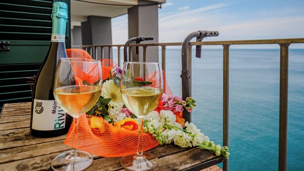 A table with a bottle of wine, two glasses, and a bouquet of flowers on a balcony overlooking the sea. - Il Baluardo Sea View Apartment on the Cliff (Riomaggiore)