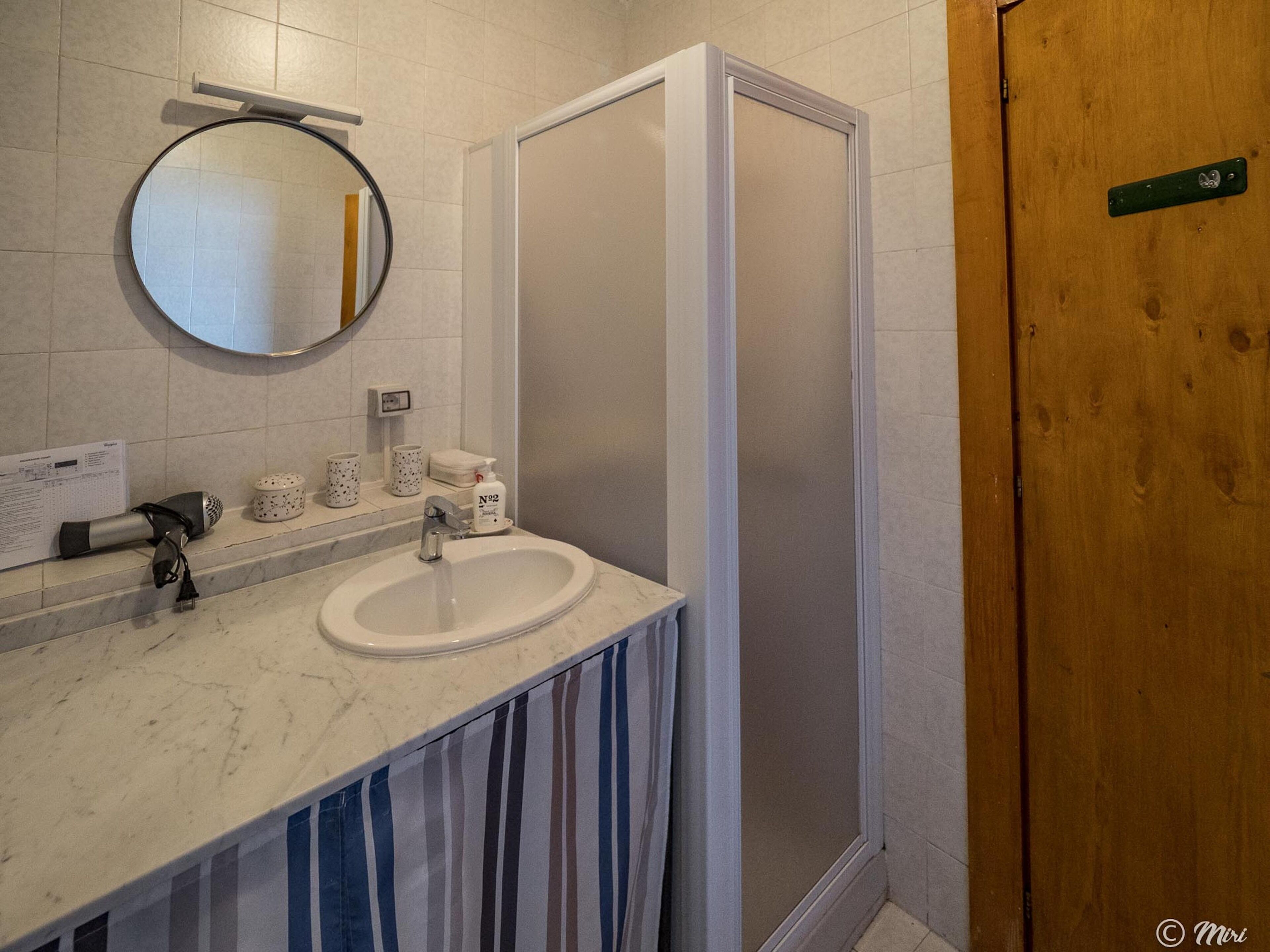 Een badkamer met een witte wastafel, een spiegel en een douchecabine.