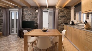 A modern kitchen with wooden cabinets, a dining table with chairs, a television, and a stone wall. - Casa do Leme - Rustic House (Funchal- Madeira)