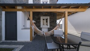 A covered outdoor seating area with a stone wall, a hammock, and a table with chairs. - Casa do Leme - Rustic House (Funchal- Madeira)
