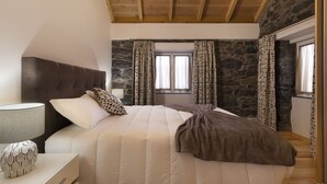 A bedroom with a bed, a nightstand, a lamp, and a stone wall. - Casa do Leme - Rustic House (Funchal- Madeira)