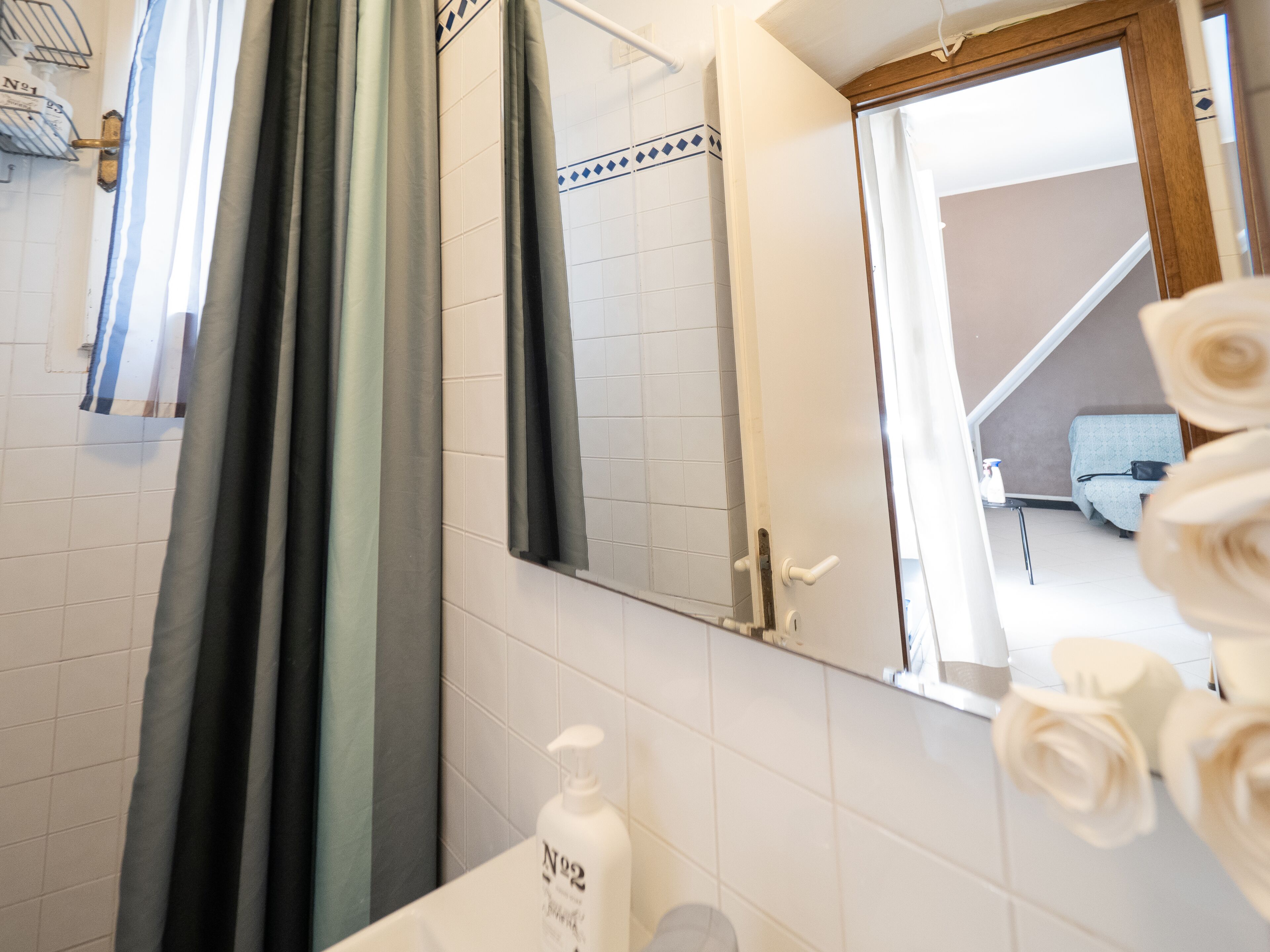 A bathroom with a mirror, a towel rack, a shower curtain, and a bottle of soap.