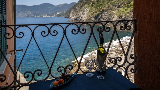 Uma varanda com vista para o mar, uma garrafa e dois copos sobre uma mesa.