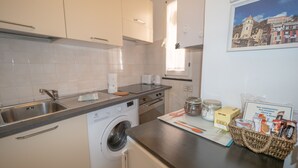 Cozinha compacta com máquina de lavar, pia e bancada com cesta de itens para o café da manhã.