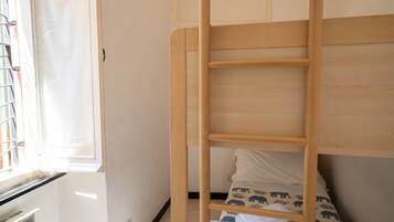 Een stapelbed met een houten trap, een raam met luiken en een radiator.