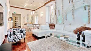 A modern living room with a white sectional sofa, a glass coffee table, and a decorative tree branch on the wall. - MONTEVERDE GUESTHOUSE: Spacious Villa in Rome Center ! (Roma)