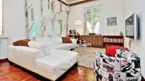 A modern living room with a white sofa, a glass coffee table, and a bookshelf. - MONTEVERDE GUESTHOUSE: Spacious Villa in Rome Center ! (Roma)