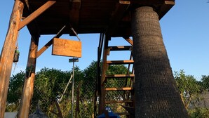 Une cabane en bois perchée dans un arbre, dotée d’une fenêtre et de deux jardinières suspendues.