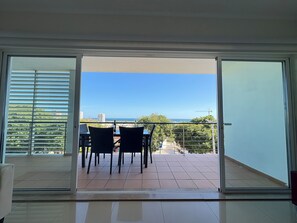 A balcony with a table and chairs, a view of the sea, and a cityscape in the background.