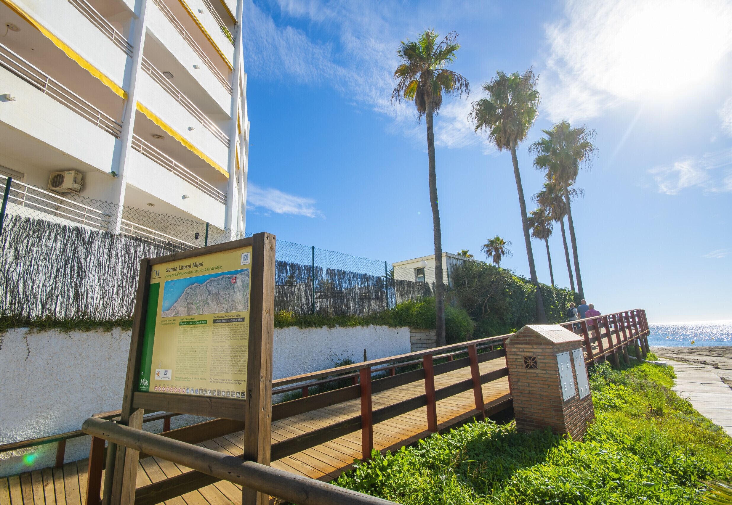 Une promenade en bois menant à une plage bordée de palmiers et à un bâtiment doté de balcons.