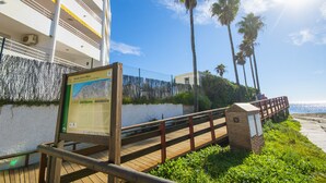 A wooden boardwalk leading to a beach with palm trees and a building with balconies. - Cubo's Apartamento Tarajes La Cala / free wifi / air conditioning (Mijas Costa)