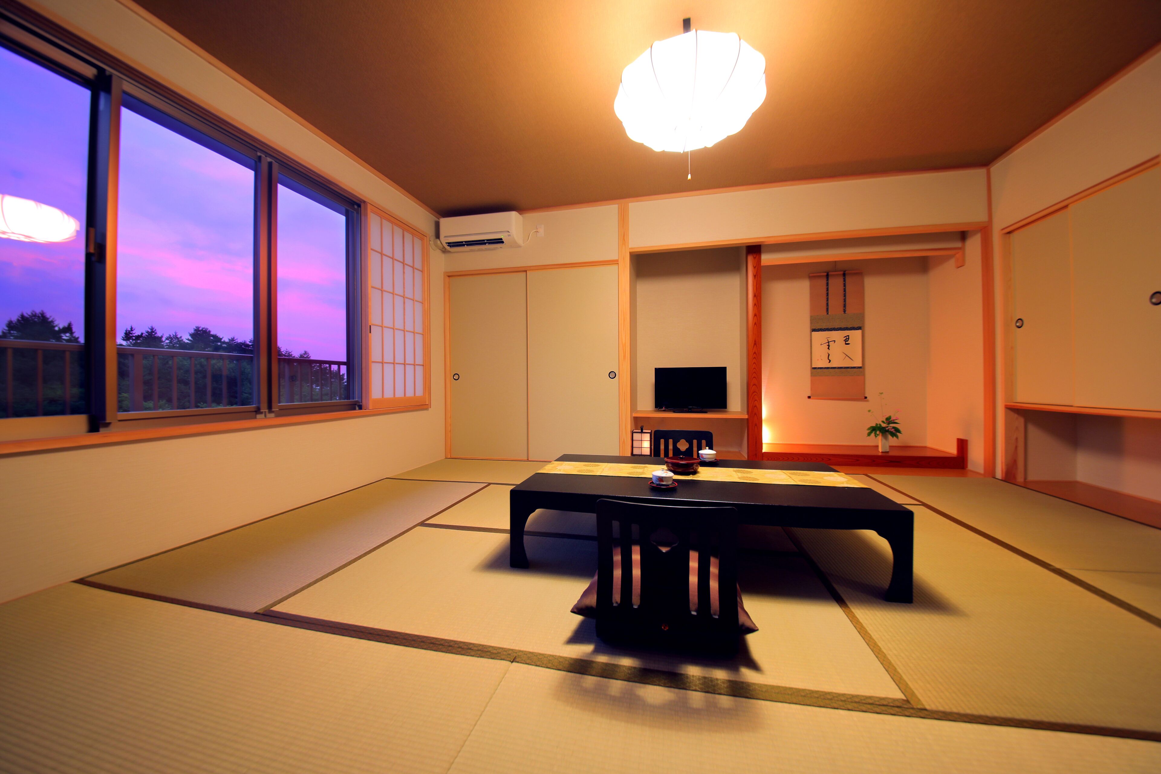 Um quarto japonês tradicional com tatames, uma mesa baixa e uma televisão.