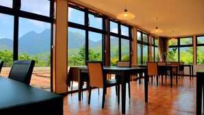 A spacious dining area with large windows offering a mountain view. Tables and chairs are arranged for dining. - Kuju Kanko Hotel (Kokonoe)